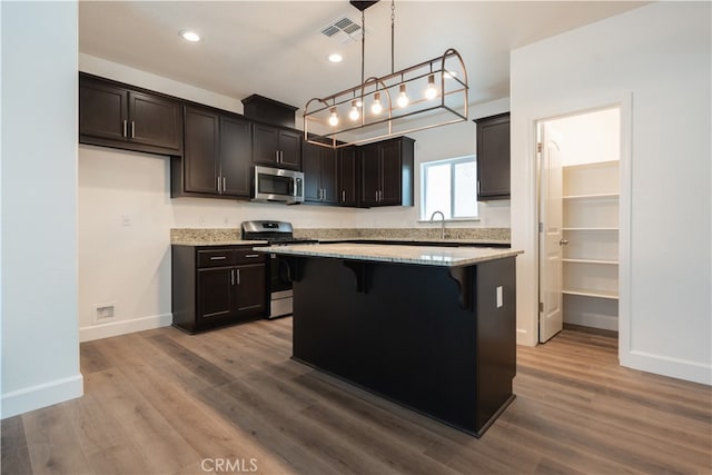 kitchen featuring a kitchen island, hanging light fixtures, hardwood / wood-style floors, stainless steel appliances, and a breakfast bar