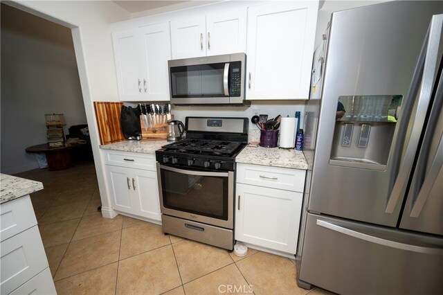 kitchen featuring light stone counters, white cabinets, light tile patterned flooring, and stainless steel appliances