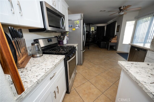 kitchen with appliances with stainless steel finishes, light tile patterned flooring, white cabinets, light stone countertops, and ceiling fan