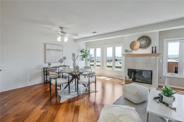 dining space with a tiled fireplace, wood-type flooring, and ceiling fan