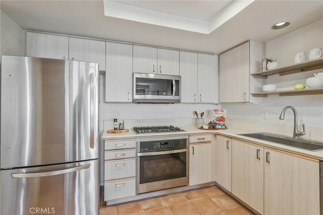 kitchen with appliances with stainless steel finishes, sink, light tile patterned floors, and a tray ceiling