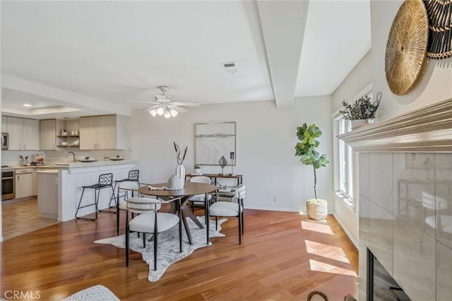 dining area with ceiling fan, beam ceiling, hardwood / wood-style floors, and a fireplace