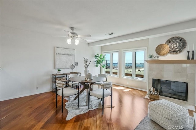 dining space with a tile fireplace, wood-type flooring, and ceiling fan