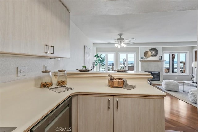 kitchen featuring a fireplace, light brown cabinetry, dishwasher, ceiling fan, and kitchen peninsula