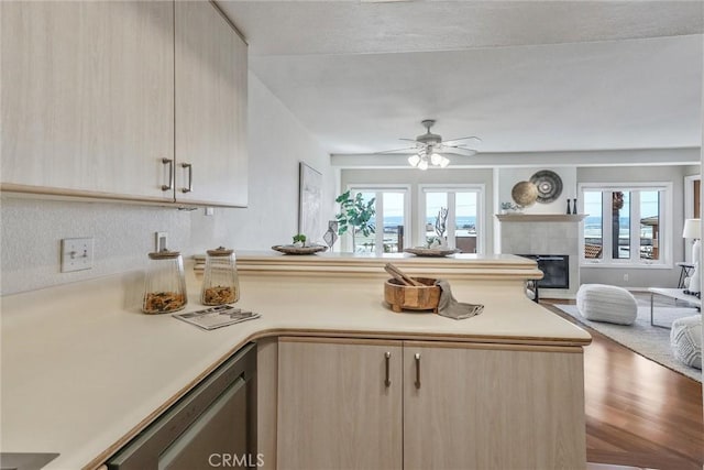 kitchen featuring light brown cabinetry, stainless steel dishwasher, a tile fireplace, ceiling fan, and hardwood / wood-style floors