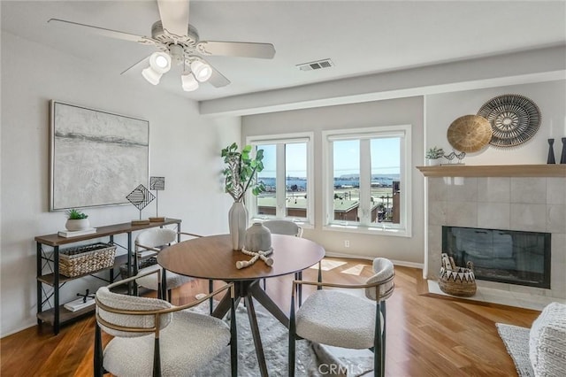 dining room featuring ceiling fan, wood-type flooring, and a tiled fireplace