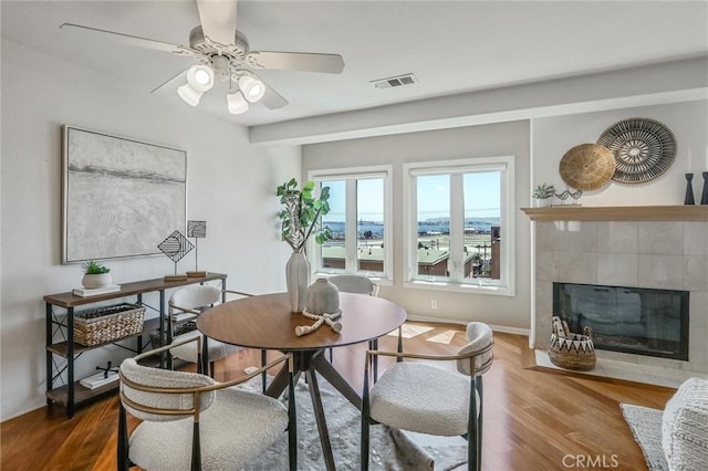 dining room with a tile fireplace, wood-type flooring, and ceiling fan