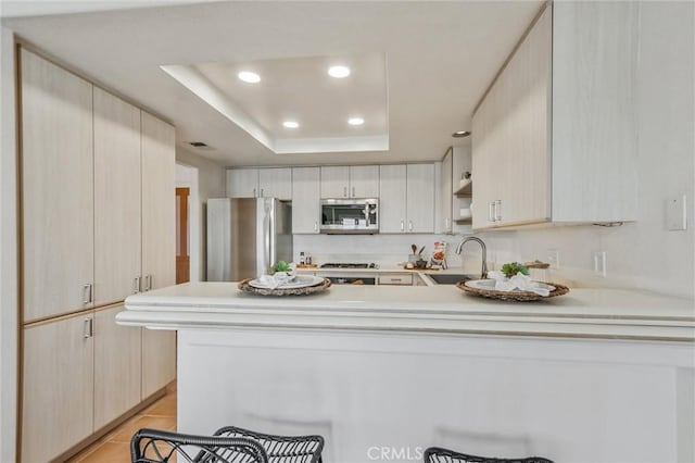 kitchen with a tray ceiling, sink, light tile patterned floors, kitchen peninsula, and stainless steel appliances