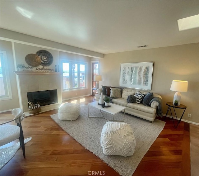 living room featuring wood-type flooring, a fireplace, and a skylight