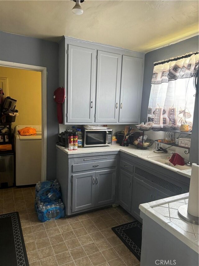 2016 W 103rd St, Los Angeles, CA 90047 - kitchen featuring stainless steel microwave, washer / clothes dryer, light countertops, and gray cabinetry