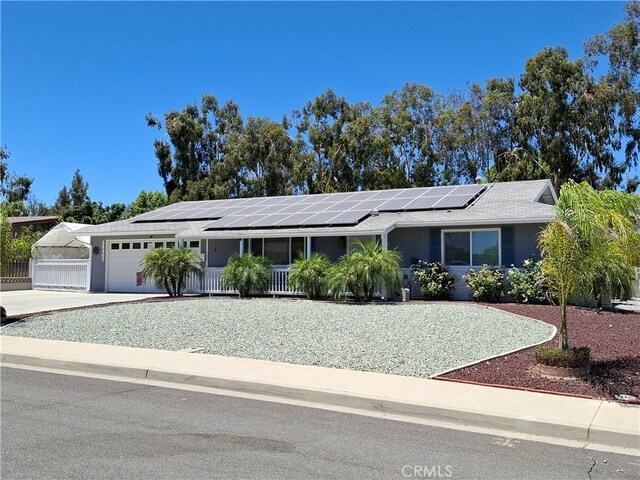 ranch-style home featuring covered porch, solar panels, and a garage