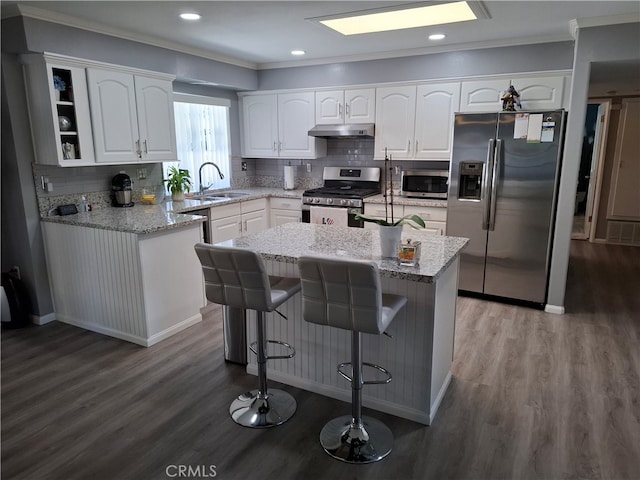 kitchen featuring sink, appliances with stainless steel finishes, a kitchen island, light stone counters, and white cabinetry