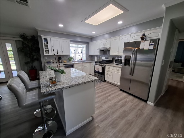 kitchen featuring light stone countertops, appliances with stainless steel finishes, sink, white cabinetry, and a breakfast bar area