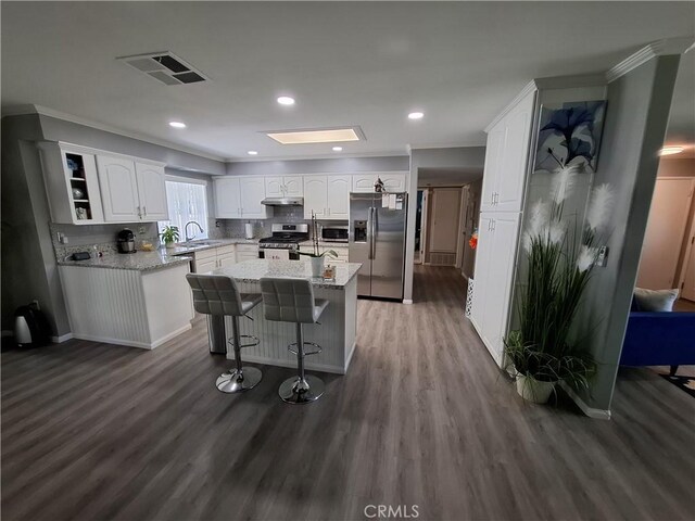 kitchen featuring white cabinetry, stainless steel appliances, light stone counters, a kitchen bar, and a kitchen island