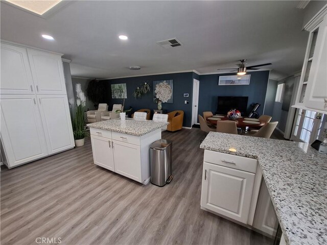 kitchen with ceiling fan, ornamental molding, a kitchen island, light stone counters, and white cabinetry