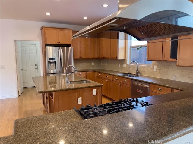 kitchen with sink, appliances with stainless steel finishes, light wood-type flooring, and an island with sink