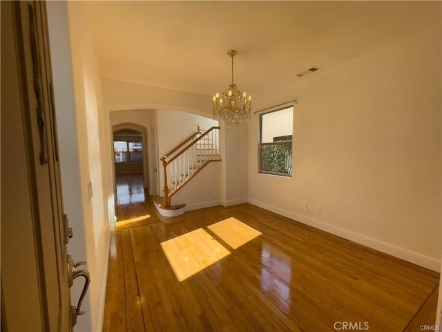 empty room with hardwood / wood-style flooring and an inviting chandelier