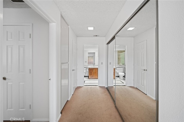 hallway featuring a textured ceiling and light colored carpet