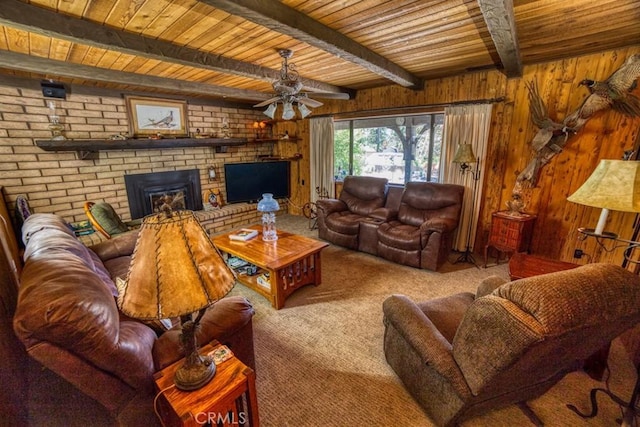 living room with wood walls, a brick fireplace, ceiling fan, beamed ceiling, and carpet floors