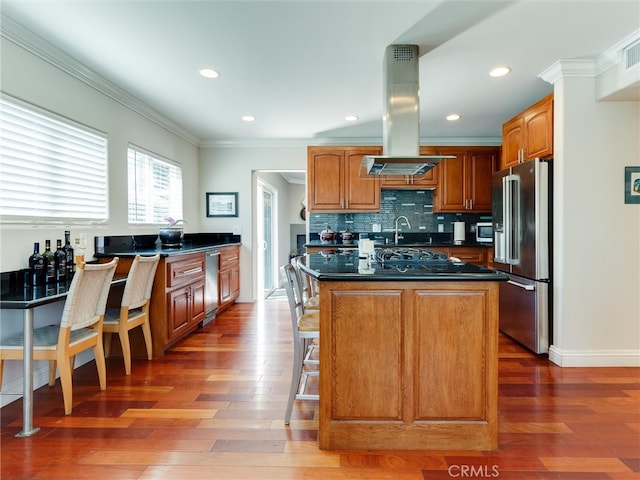 kitchen featuring island range hood, a center island with sink, appliances with stainless steel finishes, dark hardwood / wood-style flooring, and decorative backsplash