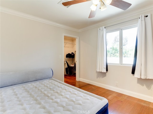 bedroom featuring a closet, hardwood / wood-style floors, crown molding, a spacious closet, and ceiling fan