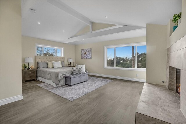 bedroom with beam ceiling, light wood-type flooring, multiple windows, and a tiled fireplace