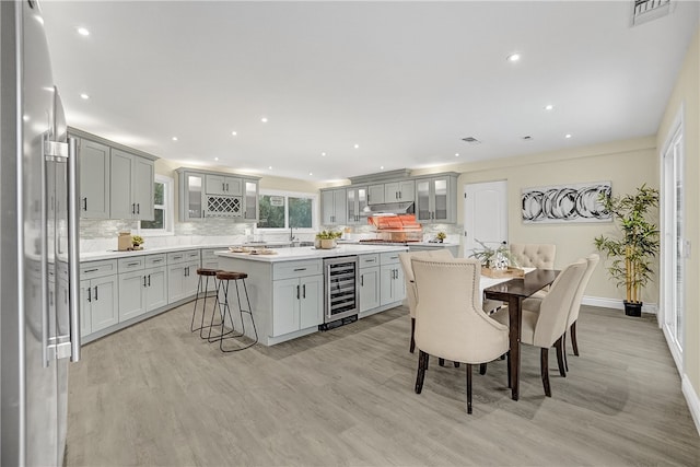 kitchen with a breakfast bar, refrigerator, light wood-type flooring, a kitchen island, and beverage cooler