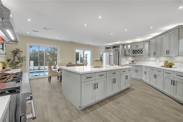 kitchen featuring a center island, wall chimney exhaust hood, tasteful backsplash, light hardwood / wood-style flooring, and stainless steel built in refrigerator