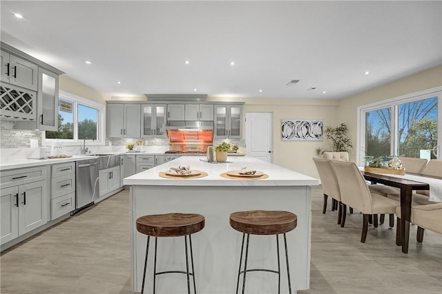 kitchen with stainless steel appliances, a breakfast bar area, gray cabinets, decorative backsplash, and a kitchen island