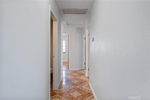 hall featuring attic access and baseboards