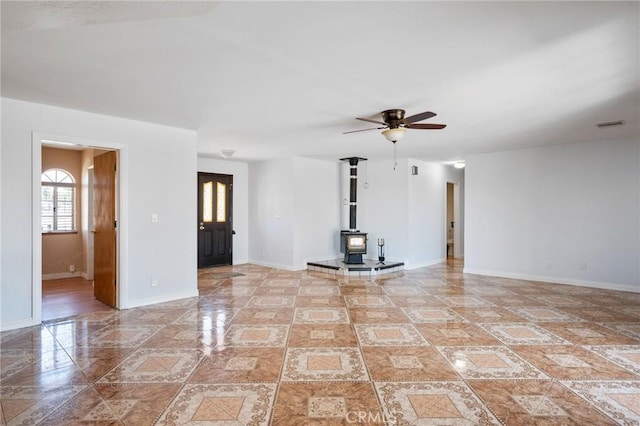 unfurnished living room with a wood stove and ceiling fan