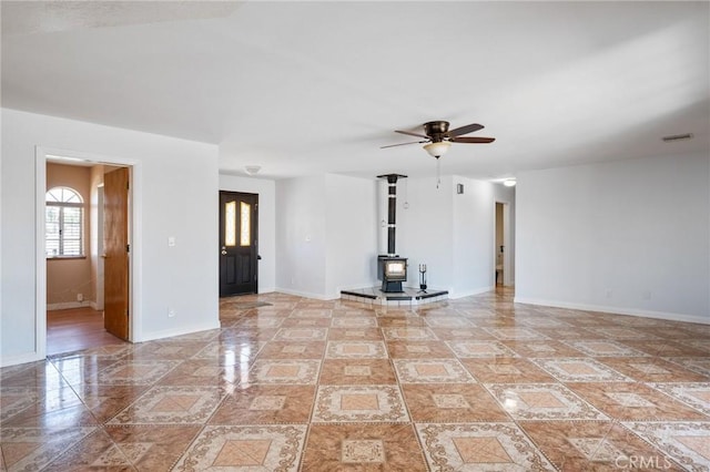 unfurnished living room featuring a wood stove, ceiling fan, visible vents, and baseboards