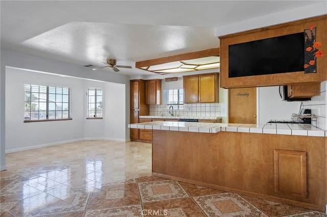 kitchen with ceiling fan, sink, backsplash, tile countertops, and kitchen peninsula