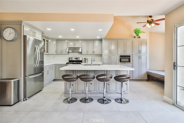 kitchen featuring appliances with stainless steel finishes, light tile patterned flooring, decorative backsplash, and a center island with sink