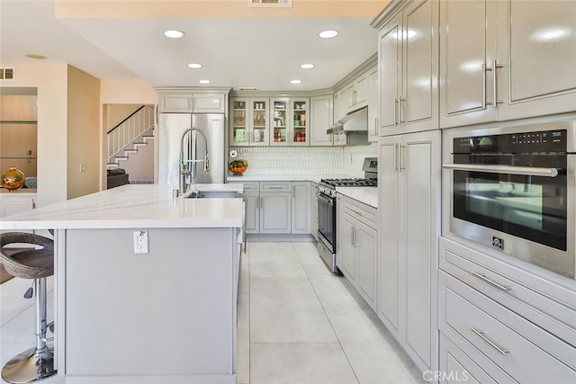 kitchen featuring appliances with stainless steel finishes, sink, light tile patterned floors, decorative backsplash, and an island with sink