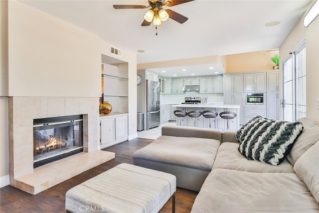 living room with dark hardwood / wood-style floors, a tiled fireplace, built in features, and ceiling fan