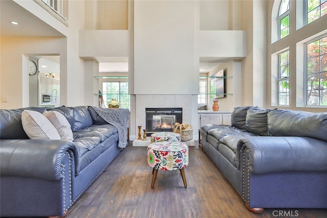 living room featuring a healthy amount of sunlight, a tiled fireplace, dark hardwood / wood-style flooring, and a high ceiling