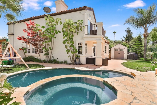 rear view of property with a balcony, a patio, a pool with hot tub, and a shed