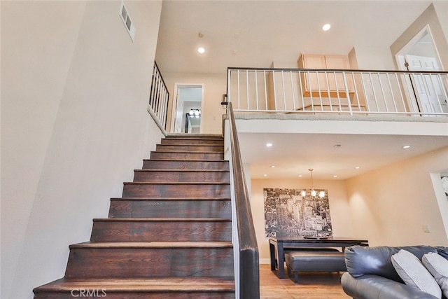 stairs with a notable chandelier, light wood-type flooring, and a towering ceiling