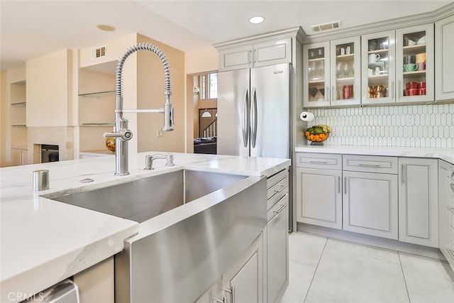 kitchen with gray cabinetry, stainless steel fridge, light stone counters, backsplash, and light tile patterned floors