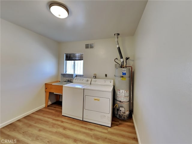 washroom featuring washing machine and dryer, strapped water heater, and light hardwood / wood-style flooring