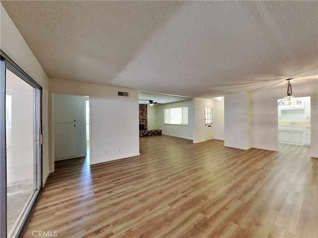 unfurnished living room featuring a textured ceiling, a brick fireplace, light hardwood / wood-style flooring, and ceiling fan