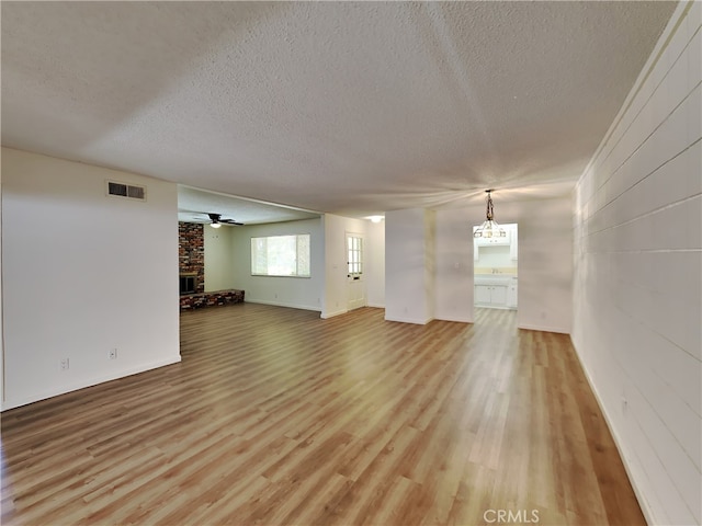 unfurnished living room with a textured ceiling, brick wall, a fireplace, ceiling fan, and hardwood / wood-style flooring