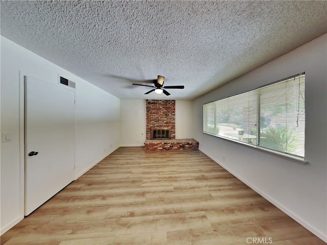 unfurnished living room with light wood-type flooring, a brick fireplace, a textured ceiling, and ceiling fan