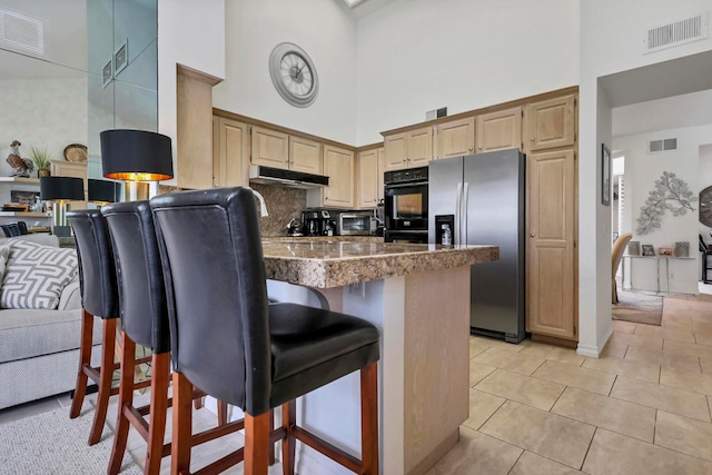 kitchen featuring a kitchen breakfast bar, stainless steel fridge, a high ceiling, and light tile patterned floors