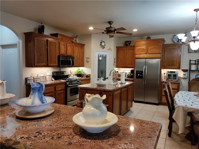 kitchen featuring hanging light fixtures, light tile patterned floors, a kitchen island with sink, stainless steel appliances, and ceiling fan with notable chandelier