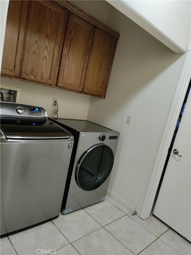 clothes washing area with washer and clothes dryer, light tile patterned floors, and cabinets