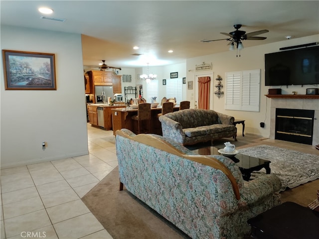 living room featuring ceiling fan with notable chandelier, a tiled fireplace, and light tile patterned floors