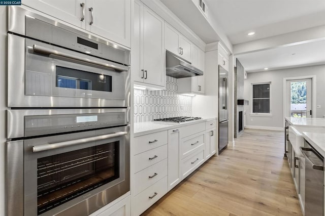 kitchen with light stone counters, backsplash, white cabinets, and appliances with stainless steel finishes