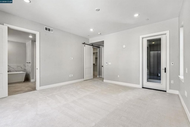 unfurnished bedroom with ensuite bathroom, light carpet, and a barn door